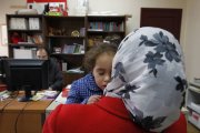 Una mujer migrante coge en el cuello a su hija dormida.