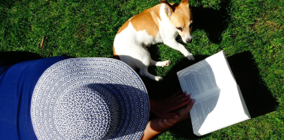 Una mujer lee en una zona verde acompañada de su mascota.