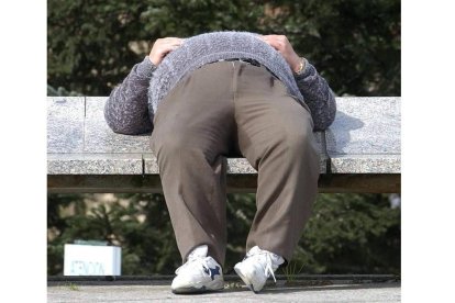 Una persona aprovecha el sol para dormir una siesta en un banco de una calle.