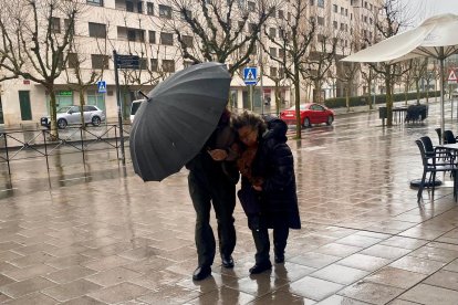Dos personas caminan por la calle en León en pleno temporal de lluvia y viento