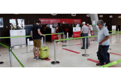 Los primeros pasajeros facturando ayer en el Aeropuerto de León, cumpliendo las distancias de seguridad. FERNANDO OTERO