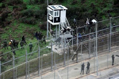 Varios inmigrantes custodiados por la policia marroquí junto a la valla de Ceuta.