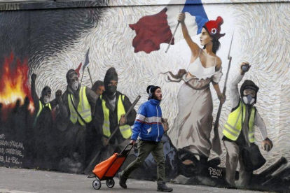 Un hombre pasa junto a un mural que reproduce una versión de La libertad guiando al pueblo, de  Eugene Delacroix, con la presencia de chalecos amarillos, idea del artista Pascal Boyart.