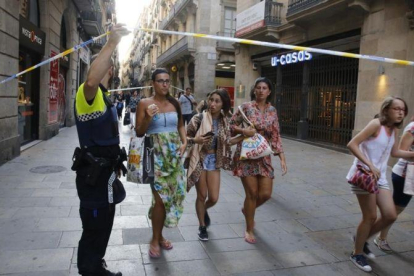 Unos turistas pasan bajo un cordón policial en la calle de Portaferrissa.