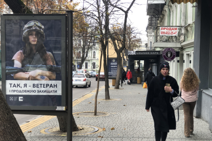 Una mujer pasea ante un cartel de una joven militar y armada. GERVASIO SÁNCHEZ