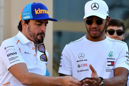Alonso consulta un móvil junto a Hamilton en Abu Dhabi.