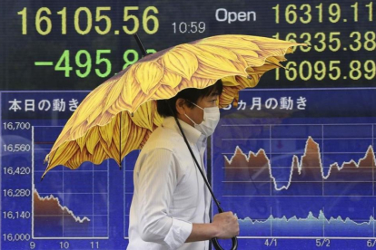 Un hombre pasa ante un sociedad de bolsa en Tokio en cuyo paneles informativos se muestra la caída del mercado.