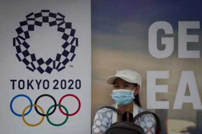 Una mujer en Bangkok, junto al cartel de los Juegos de Tokio, que se han aplazado a 2021. DIEGO AZUBEL