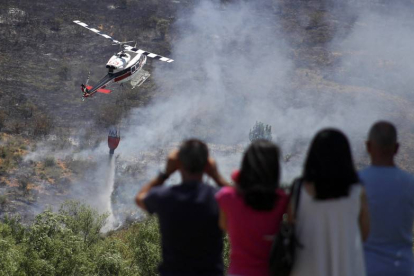 Personal de tierra y un helicóptero trabajan en las labores de extinción de un incendio forestal registrado entre las localidades de Santovenia de la Valdoncina y Fresno del Camino