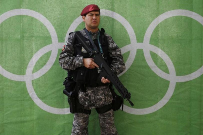 Un policía bien armado hace guardia delante de los aros olímpicos.