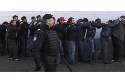 Un agente de policía vigila a varios de los inmigrantes detenidos en la redada masiva, este lunes en Moscú.