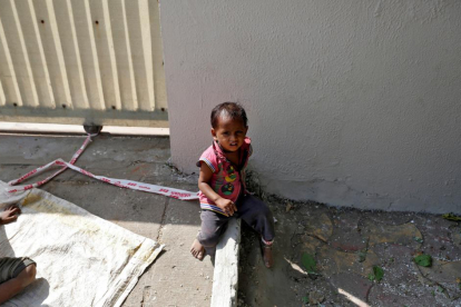 La pequeña Shivani, de 15 meses, atada con una cinta a una piedra mientras su madre trabaja.
