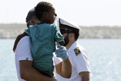 Un medico tiene en brazo un niño desembarcado del barco de la Guardia de Finanza en Pozzallo, Sicilia /
