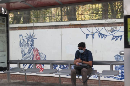 Un iraní espera en la parada de autobús junto a un mural contrario a Estados Unidos. MARINA VILLÉN