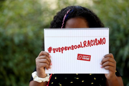 La pequeña que sufrió el acoso de sus compañeras sujeta el cartel de la campaña #suspensoalRACISMO, lanzada fechas atrás en redes sociales. EFE/ Sebastián Mariscal