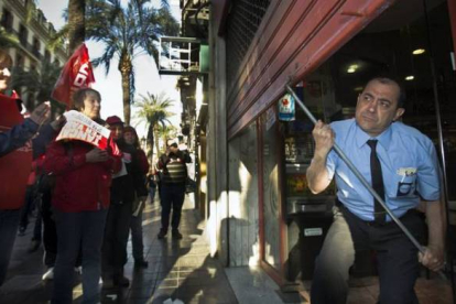 Un trabajador baja la persiana de una cafetería al paso de un piquete de sindicatos en Valencia. Foto: MIGUEL LORENZO