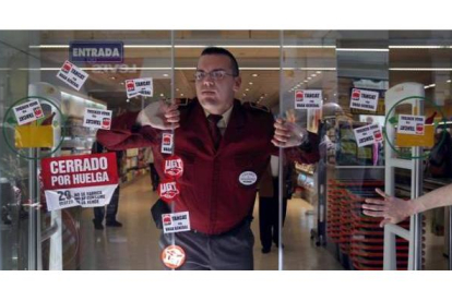 Un vigilante de seguridad de un supermercado Mercadona de Valencia abre las puertas repletas de pegatinas. Foto: MIGUEL LORENZO