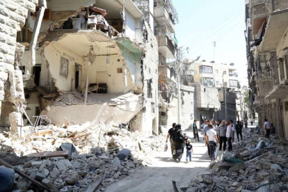 Vecinos de Alepo pasan junto a un edificio destruido en un bombardeo del régimen, este domingo.