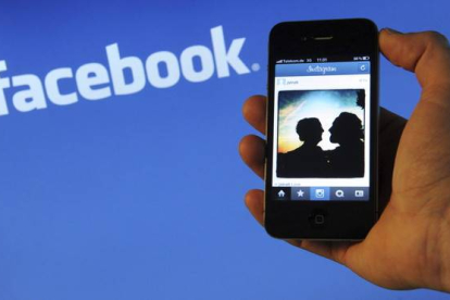 Un usuario de smartphone, delante de un logotipo de Facebook.