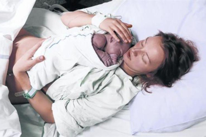 Una mujer acaricia a su hijo recién nacido en la cama de un hospital.