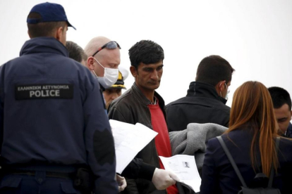 Un funcionario de la UE sostiene la documentación de un migrante (centro) en un barco que les traslada de regreso a Turquía desde Lesbos, este viernes.