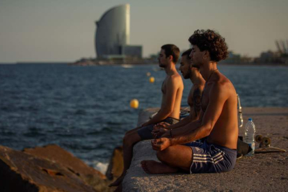 Tres jóvenes practican yoga al atardecer y frente al mar en el popular espigón del Gas de Barcelona. ENRIC FONTCUBERTA