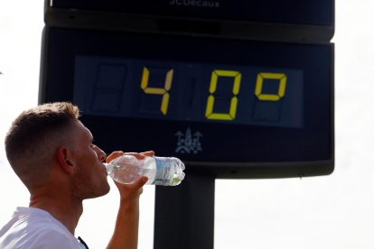 Un joven bebe agua junto a un termómetro de calle que marca 40 grados. EFE/SALAS