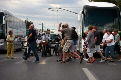 Un grupo de visitantes cruzan una calle de Atenas (Grecia) y saludan a los vehículos y motos que permanecen detenidos.