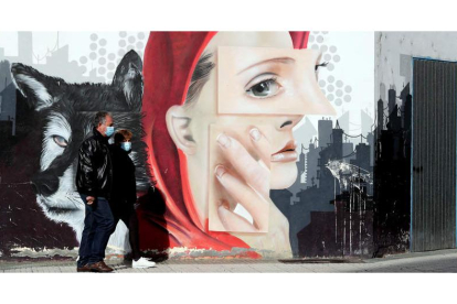 Una pareja, ayer por la mañana caminando por una calle de Ponferrada frente a un grafiti en el día del confinamiento perimetral. ANA F. BARREDO