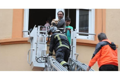 Un vecino con su perro en brazos y su hijo son evacuados del edificio por los bomberos de Ponferrada.