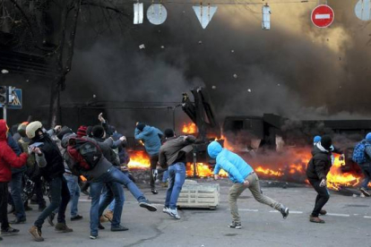 Varios manifestantes protegidos tras las barricadas lanzan piedras contra la policía ucraniana.