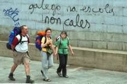 Tres peregrinos pasan delante de una pintada a favor de la enseñanza del gallego en las escuelas