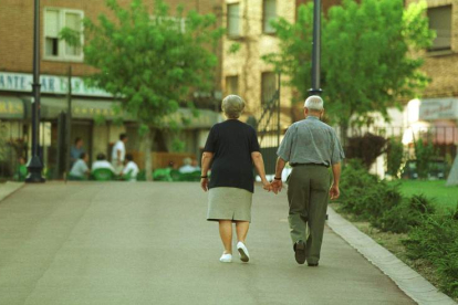 Una pareja de personas mayores pasea por un parque de León.