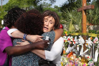 Tres mujeres se abrazan junto a la ofrenda floral frente a la iglesia metodista, en Charleston, este sábado.
