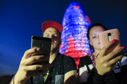 Dos personas utilizando su teléfono móvil frente a la Torre Agbar