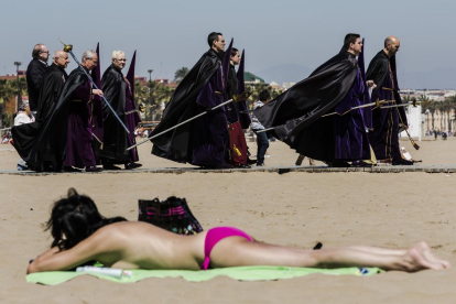 Bañistas y participantes en una procesión de Semana Santa, en la playa de Valencia.