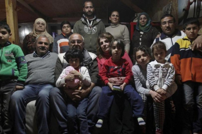 Dimitris Spiridis (en primera fila, tercero por la izquierda), junto a su mujer, Maria, y varios miembros de las dos familias sirias que acoge en su casa, en Evropos, cerca de Idomeni, este lunes.