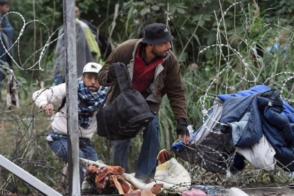 Varios migrantes cruzan la alambrada por un agujero cerca de Roszke (Hungría), en la frontera con Serbia, este jueves.
