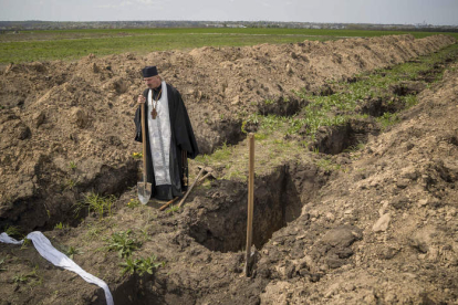 Un religioso observa las fosas en el cementerio militar de Dnipro. MIGUEL GUTIÉRREZ
