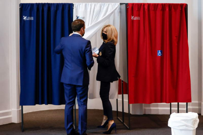 Macron y su esposa Brigitte en una cabina electoral para votar ayer en París. CHRISTIAN HARTMANN