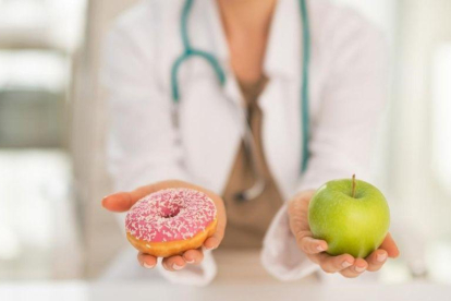 Una doctora dando a elegir entre un donut o una manzana.
