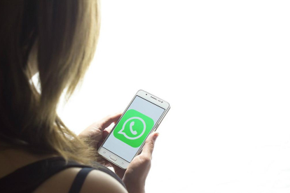 Una chica mira la pantalla de su teléfono móvil, con el logo de Whatsapp.