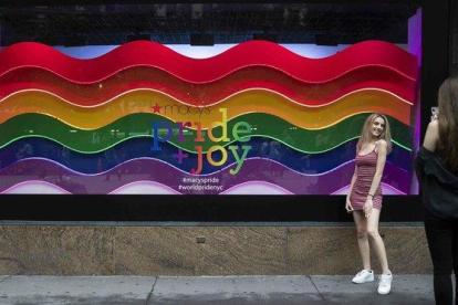 Una chica posa delante de un escaparate neoyorkino decorado con la bandera LGBTI en ocasión del día del Orgullo y el desfile del Pride.