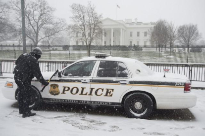 Un miembro del servicio secreto limpia la nieve de un vehículo en la Avenida Pennyslvania.