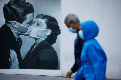 Unas personas protegidas con mascarilla pasan junto a un dibujo en la pared de un beso con mascarillas este domingo en Córdoba. SALAS