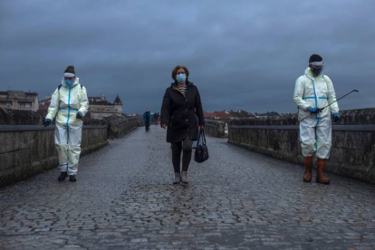 Una viandante cruza el Puente Romano de Ourense mientras empleados municipales lo desinfectan este martes. BRAIS LORENZO