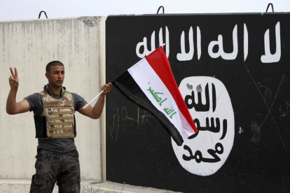 Un soldado del ejército iraquí sostiene una bandera de su país junto a la enseña del EI.