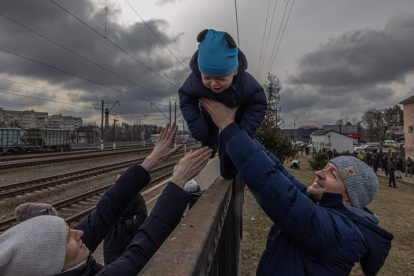 Oleg pasa por encima de una valla en Irpín a su hijo Maksim y se lo entrega a su mujer Ana antes de la llegada de un tren de evacuación a la ciudad de Kiev para salir del país. ROMAN PILIPEY