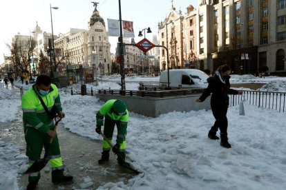 Dos operarios limpian las aceras de la calle Alcalá en Madrid mientras pasa una peatona. MARISCAL
