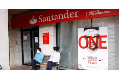 Dos mujeres charlan junto a la oficina de banco Santander que hace unos meses cerró en Riaño. CAMPOS